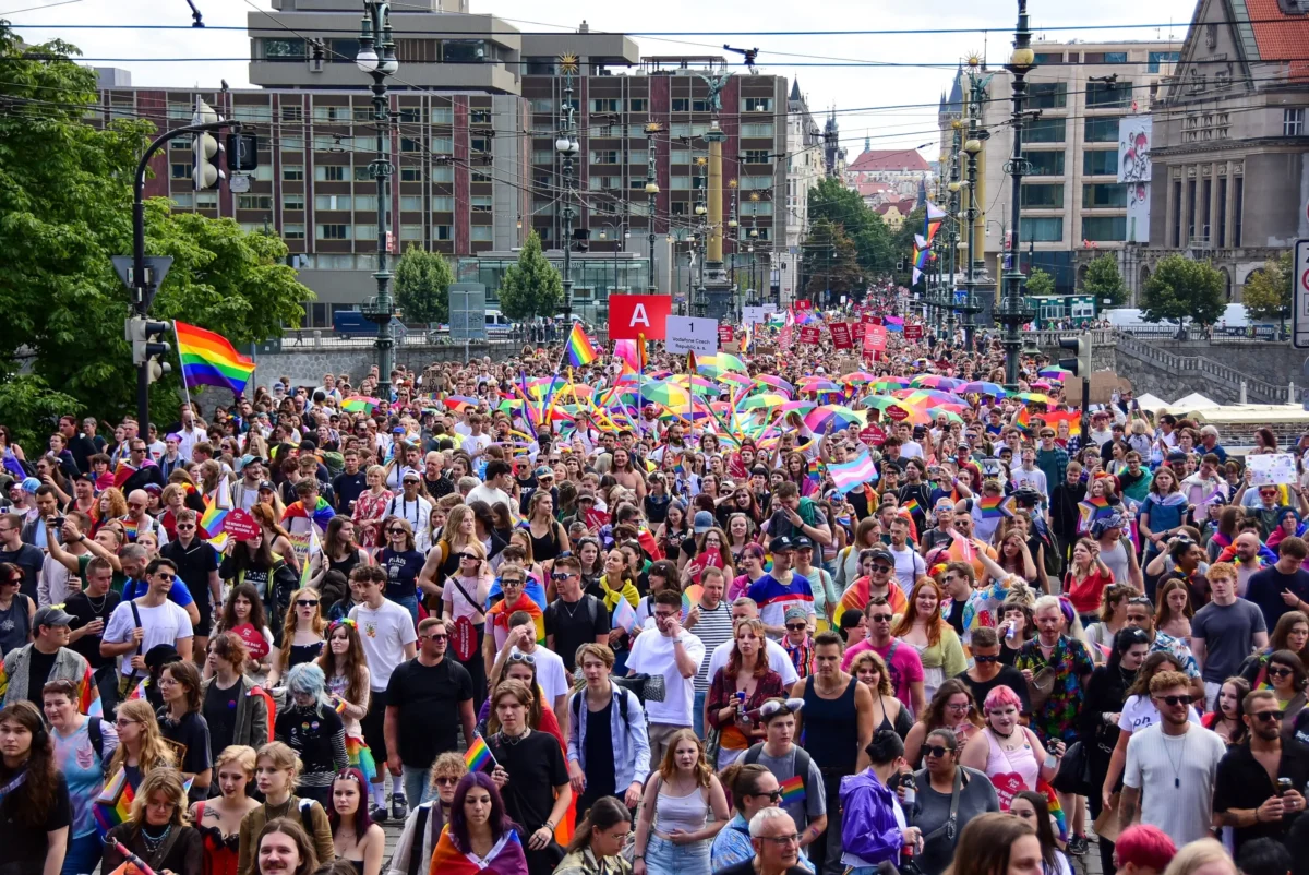 shutterstock_2661371171 1 | TVGURU.cz Large crowd at a Pride parade marching down a city street with rainbow flags and banners.
