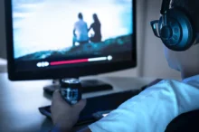 Muž má na uších sluchátka a sedí u obrazovky.