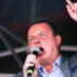 Male singer on stage, microphone in hand, raising one finger as he performs.