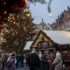 Crowded Christmas market street with a large, decorated tree and festive lights near historic buildings at dusk/evening light framing the scene