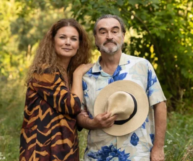 Žena stojí vedle muže a ten si před břichem drží klobouk.