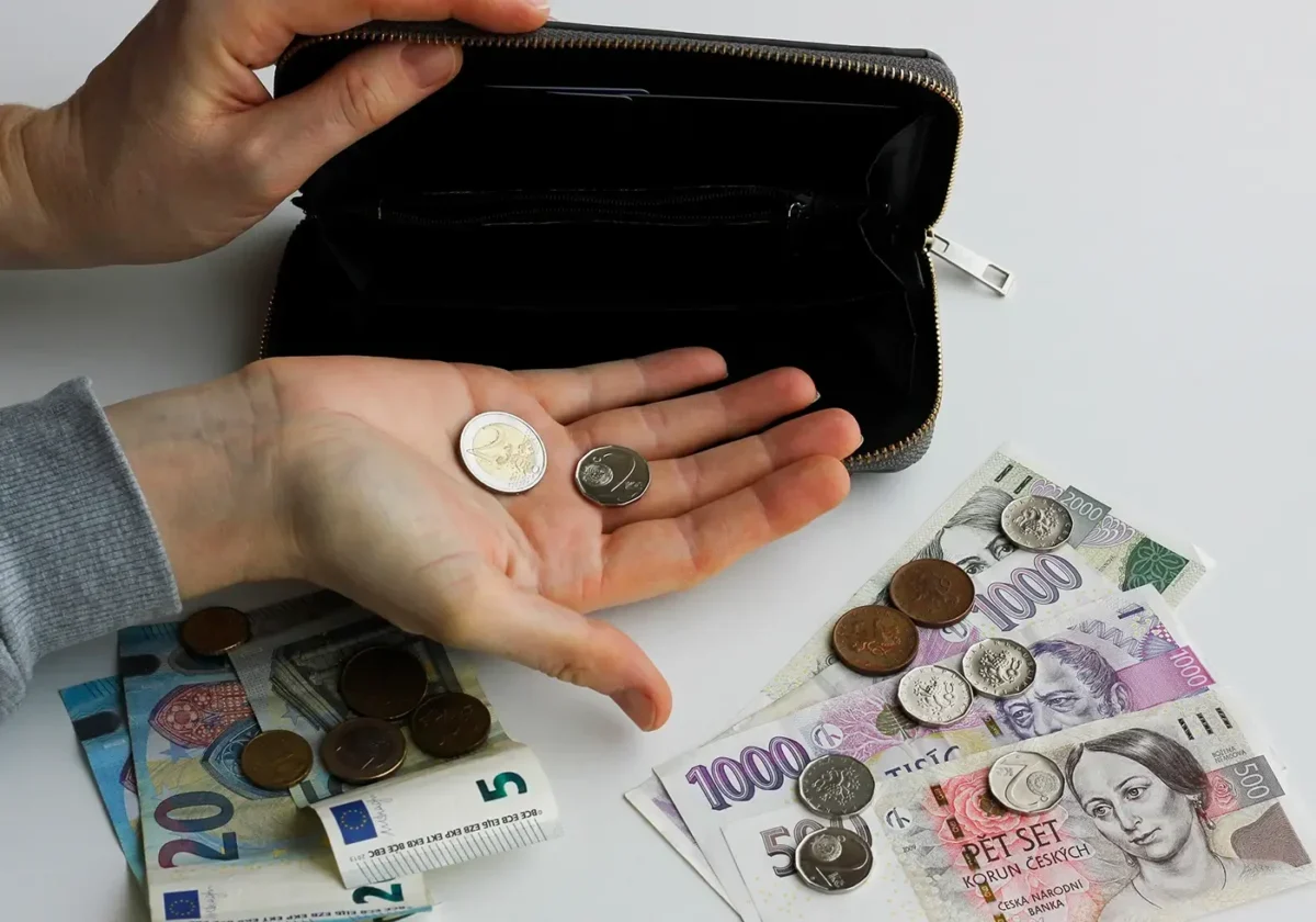Člověk v ruce drží dvě mince a na stole leží další mince a papírové bankovky