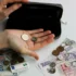 Člověk v ruce drží dvě mince a na stole leží další mince a papírové bankovky