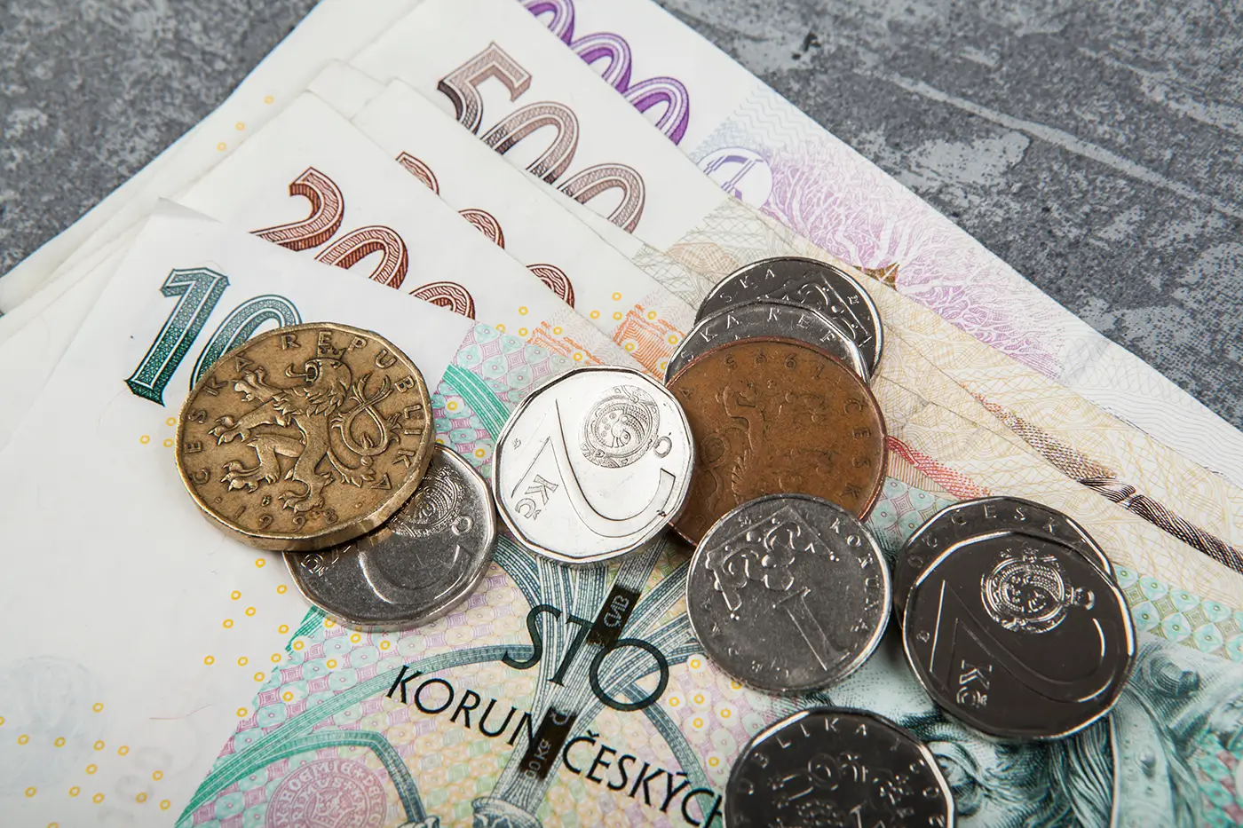 Na stole leží papírová stokoruna, dvě dvousetkoruny a pětisetkoruna a také jedna tisícikoruna a pár kovových mincí