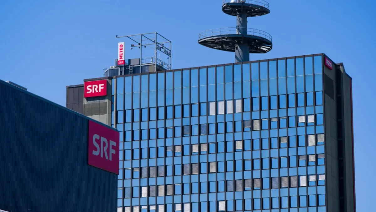 Modern glass office building with red SRF signs on the facade and a rooftop telecommunications tower against a clear blue sky.