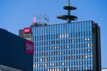 Modern glass office building with red SRF signs on the facade and a rooftop telecommunications tower against a clear blue sky.