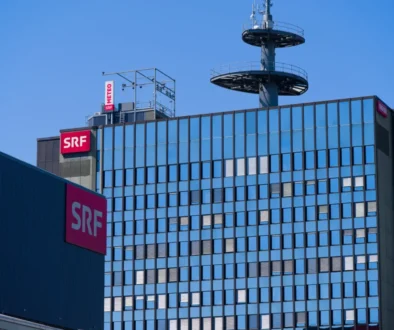 Modern glass office building with red SRF signs on the facade and a rooftop telecommunications tower against a clear blue sky.