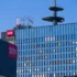 Modern glass office building with red SRF signs on the facade and a rooftop telecommunications tower against a clear blue sky.