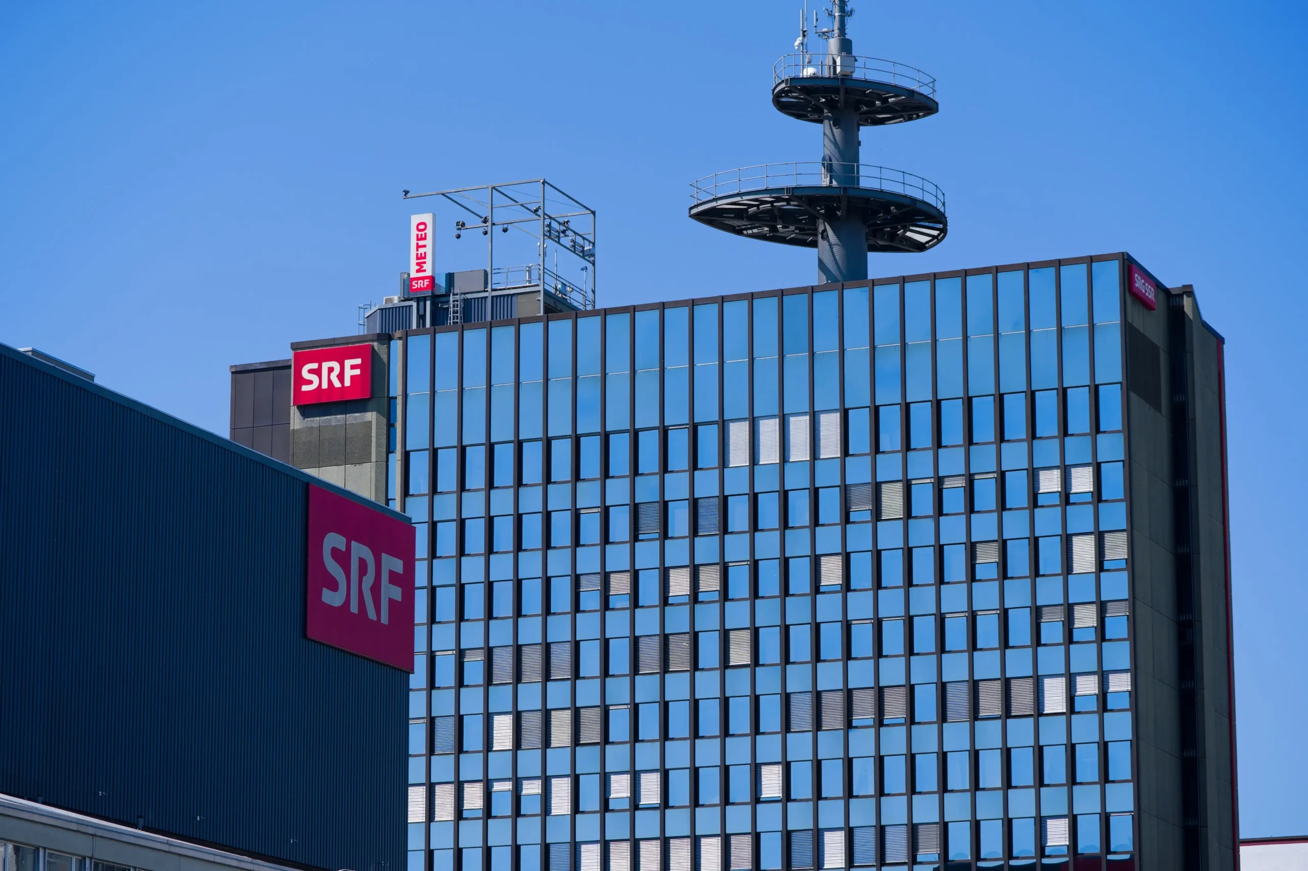 Modern glass office building with red SRF signs on the facade and a rooftop telecommunications tower against a clear blue sky.
