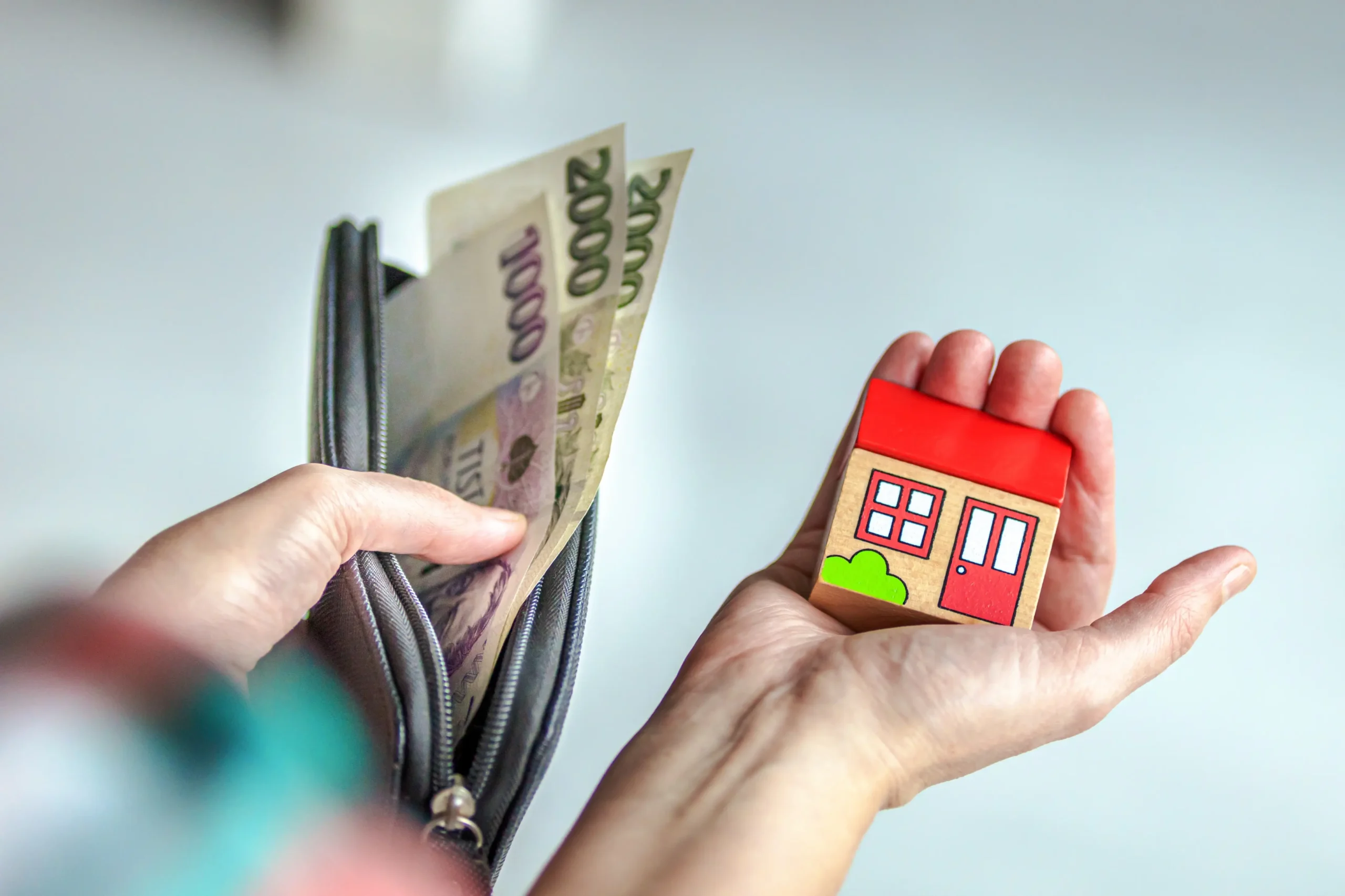 shutterstock_2653266171-2 | TVGURU.cz Osoba má v ruce české bankovky a dřevěný domeček.