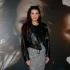 Woman wearing a black leather jacket and houndstooth skirt poses in front of a large grayscale poster backdrop.