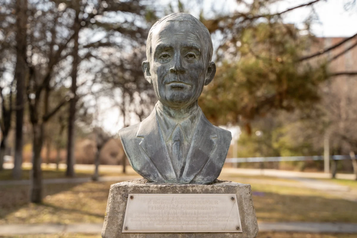 shutterstock_2266963781 1 | TVGURU.cz Bronze bust of a man in a suit on a stone pedestal in a park, with a plaque at the base.