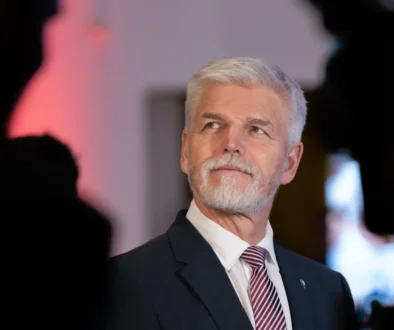 Senior man with gray hair and beard in a dark suit and red striped tie, looking to the right at a formal event.