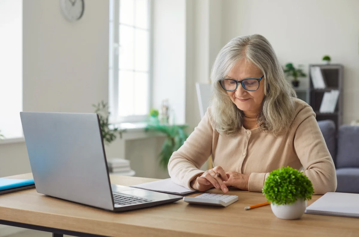 Ne každý senior dokáže se starobním důchodem vyjít. Zdroj: Shutterstock | TVGURU.cz Žena počítající na kalkulačce a sedící u počítače.