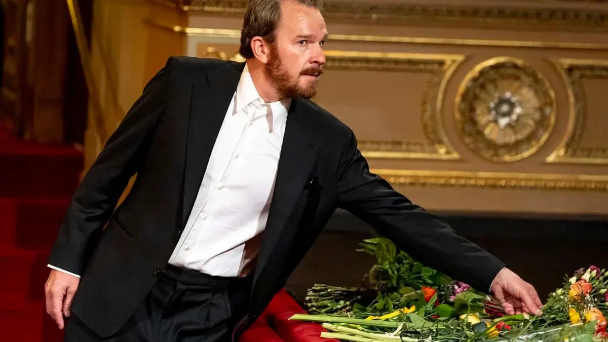 Muž v černém obleku a bílé košili pokládá na podium květiny