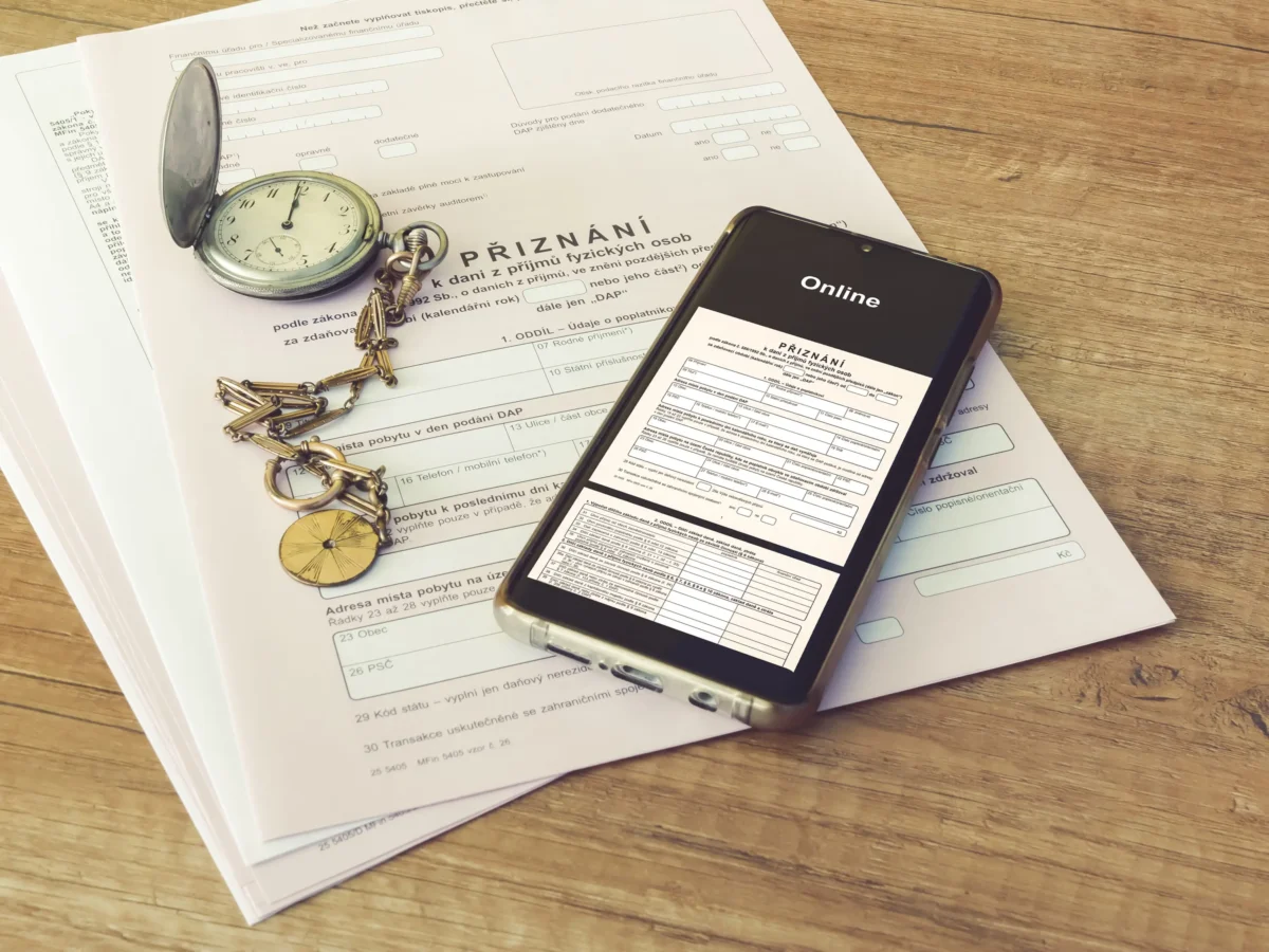 shutterstock_1924610978 1 | TVGURU.cz Open forms and a silver pocket watch on a wooden desk, with a smartphone displaying an online form.