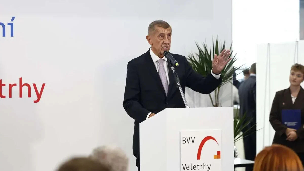 Muž stojí za bílým řečnickým pultíkem a gestikuluje