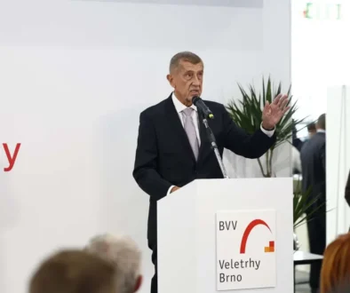 Muž stojí za bílým řečnickým pultíkem a gestikuluje