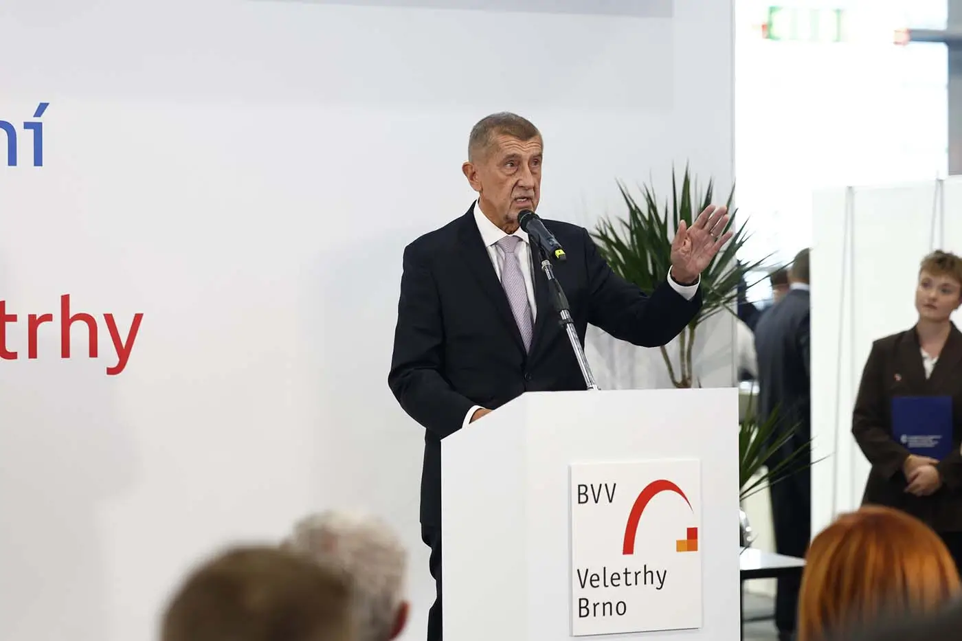 Muž stojí za bílým řečnickým pultíkem a gestikuluje