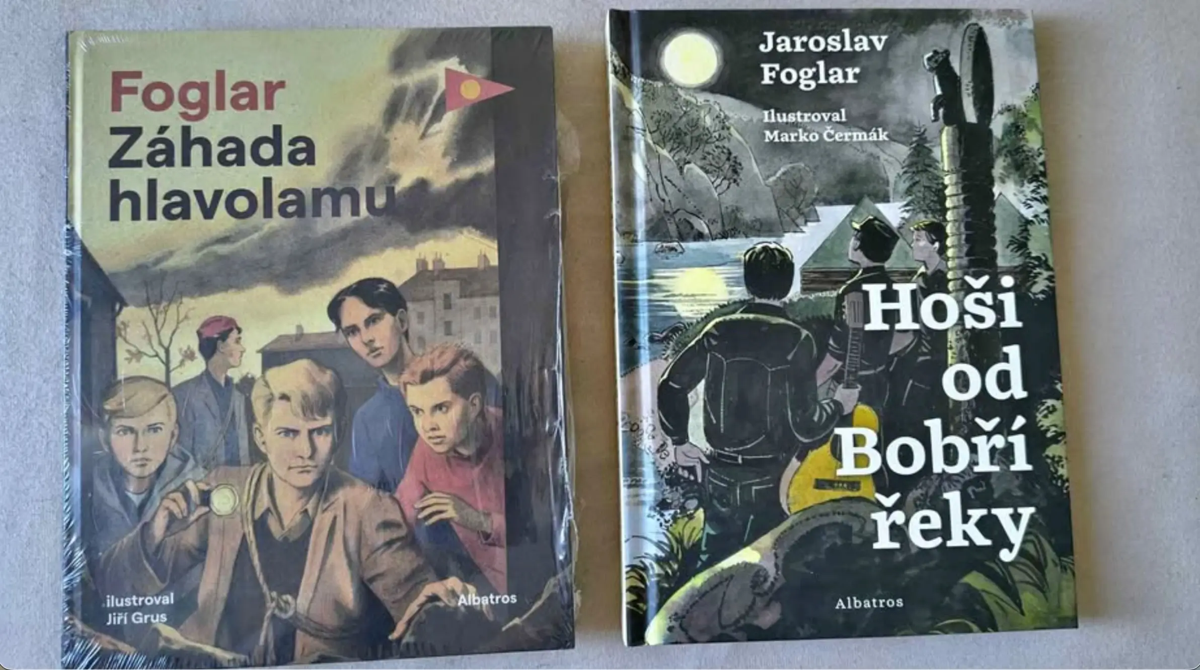 Two vintage Czech adventure paperbacks laid on a surface; left cover shows a group of boys under a cloudy sky with the title Foglar Záhada hlavolamu, right cover titled Hoši od Bobří řeky with a moonlit jungle scene.
