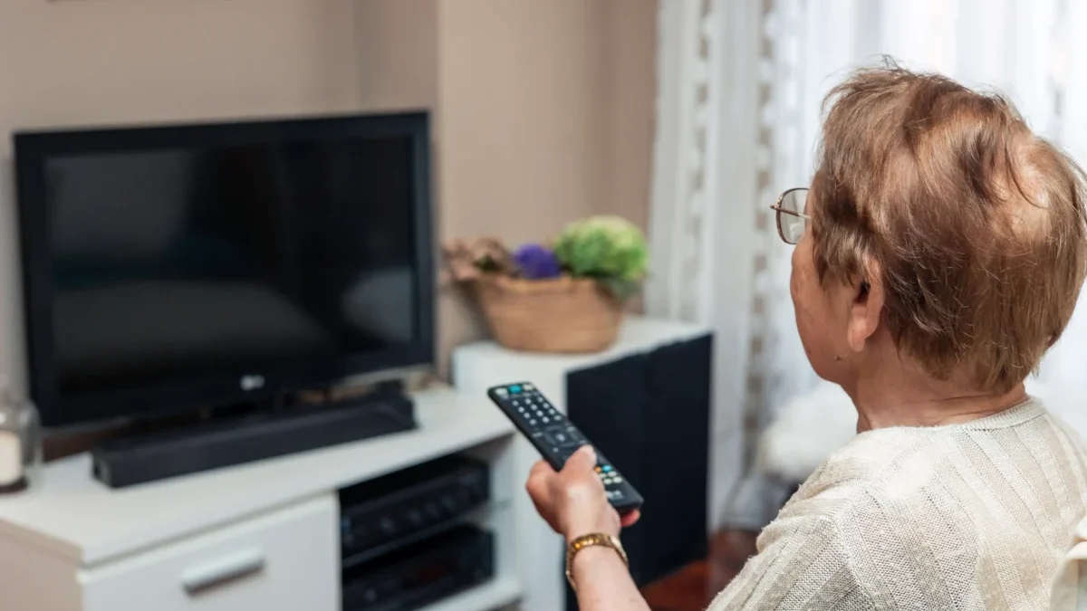 Starší žena zapíná televizi pomocí dálkového ovládání.