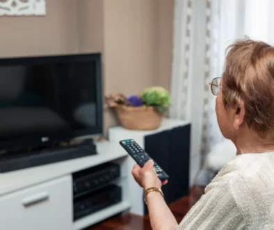 Starší žena zapíná televizi pomocí dálkového ovládání.