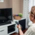 Starší žena zapíná televizi pomocí dálkového ovládání.