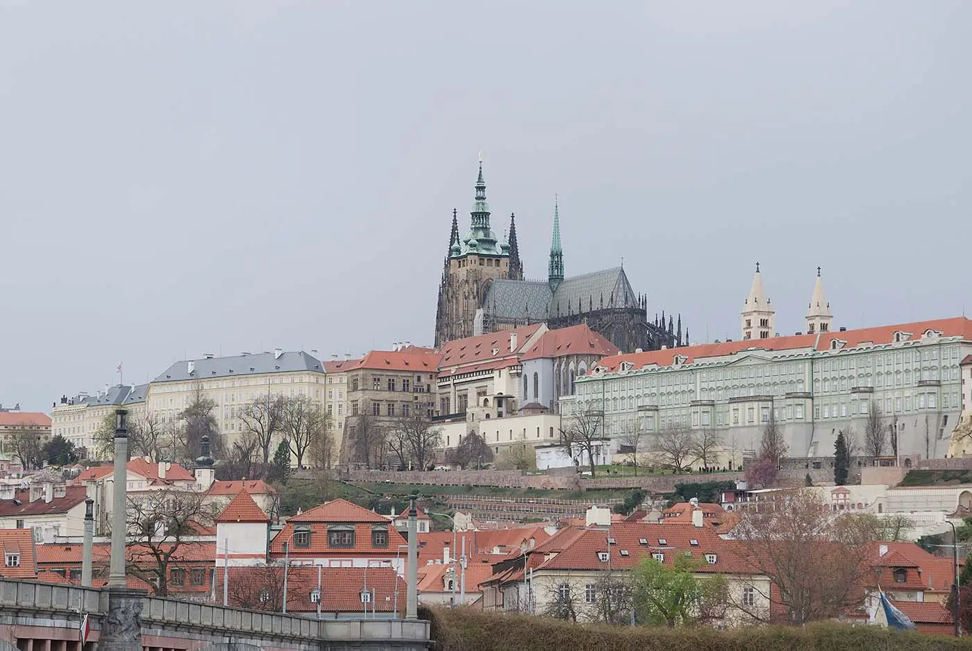 Pražský hrad s domy a stromy okolo během zataženého dne
