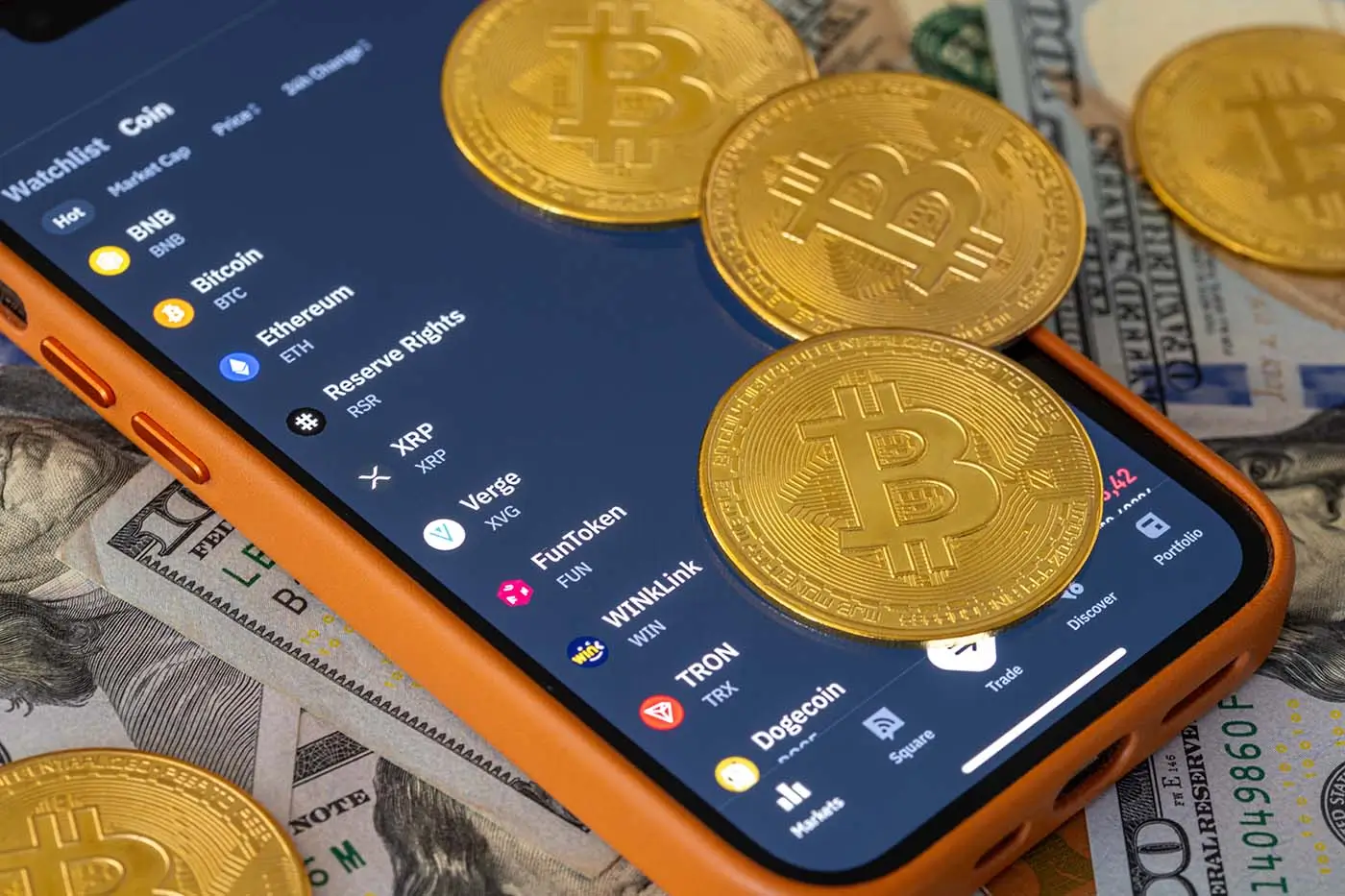 shutterstock_2568676451 | TVGURU.cz Na telefonu s otevřenou aplikací na obchodování s kryptoměnami leží několik mincí představující bitcoiny