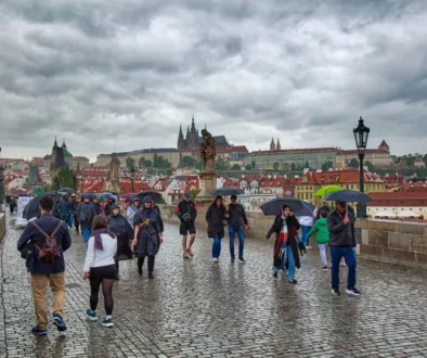Lidé v teplém oblečení a s deštníky jdou po pražském Karlově mostě