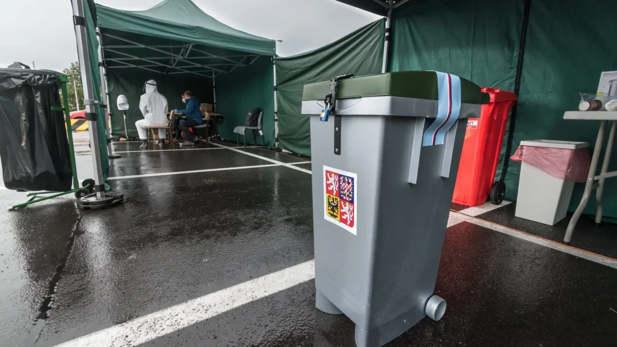 Medical testing tent with staff in PPE sitting at a table inside a green canopy structure in a parking lot.