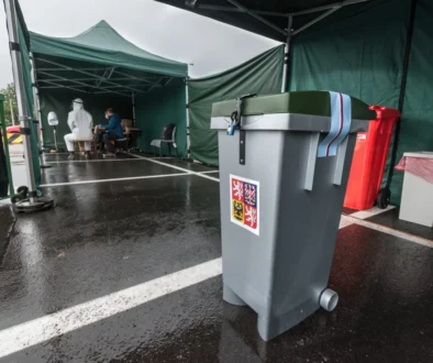 Medical testing tent with staff in PPE sitting at a table inside a green canopy structure in a parking lot.