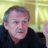 Starší muž s šedivými vlasy a šedivým knírkem na sobě má černé triko s límečkem a gestikuluje levou rukou