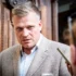 Muž ve středních letech ve světlém saku a světlé košili se dívá na někoho po svém levém boku