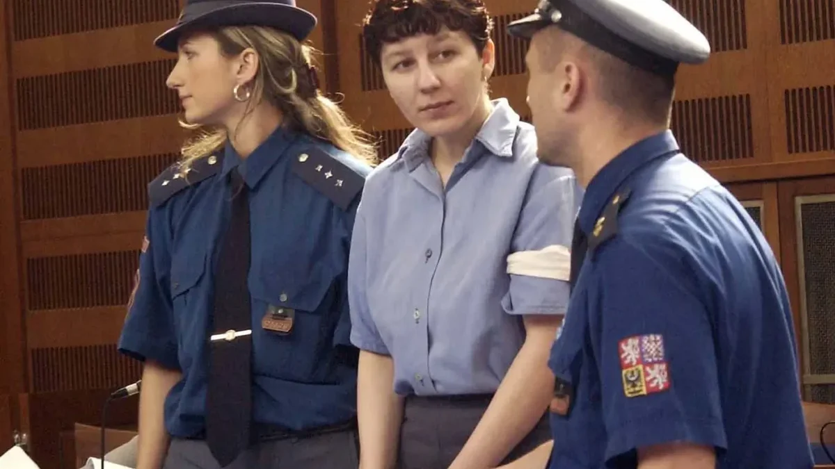 Policista a policistka zadržují ženu ve vězeňském oblečení a s pouty na rukou