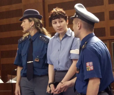 Policista a policistka zadržují ženu ve vězeňském oblečení a s pouty na rukou