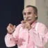 Older man with gray mustache in a pink shirt and white suspenders, smiling and clapping his hands toward the camera.