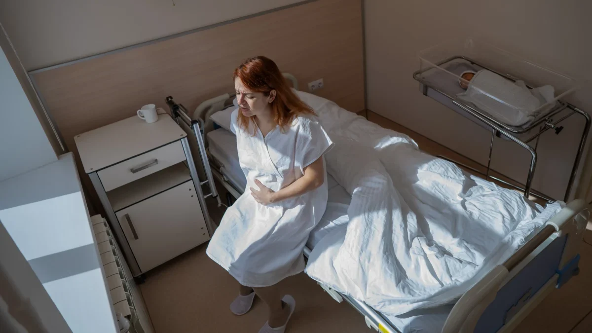 Žena sedí na posteli a vedle leží miminko.