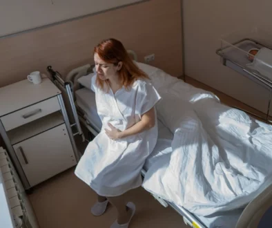 Žena sedí na posteli a vedle leží miminko.