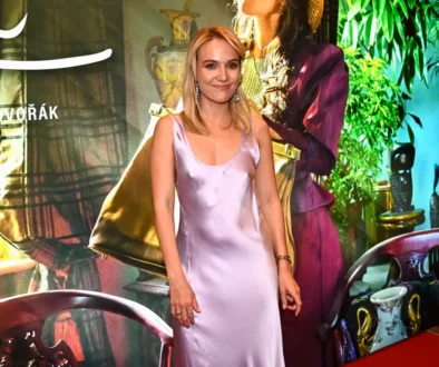 Woman in a lavender satin dress smiles at a colorful event backdrop behind her.