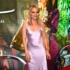 Woman in a lavender satin dress smiles at a colorful event backdrop behind her.