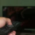 Člověk s ovladačem v ruce míří na obrazovku.