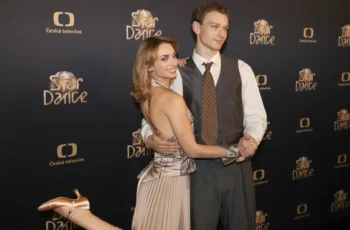 Smiling couple posing and dancing on a black backdrop with Star Dance and Česká televize logos; woman in a champagne dress and man in a gray vest and tie present on a red carpet backdrop.