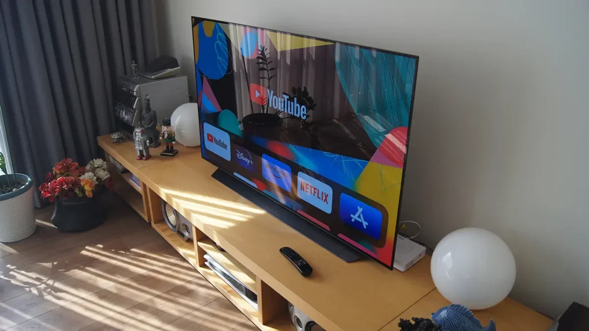 Na konferenčním stolku stojí zapnutá televize a kolem ní jsou rozmístěné různé věci