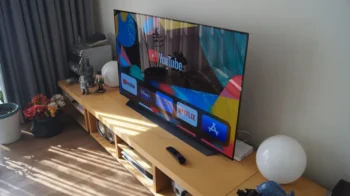Na konferenčním stolku stojí zapnutá televize a kolem ní jsou rozmístěné různé věci