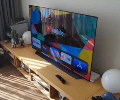 Na konferenčním stolku stojí zapnutá televize a kolem ní jsou rozmístěné různé věci