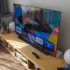 Na konferenčním stolku stojí zapnutá televize a kolem ní jsou rozmístěné různé věci