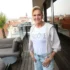Na terase běem zamračeného dne stojí starší žena v bílém tričku a džínách