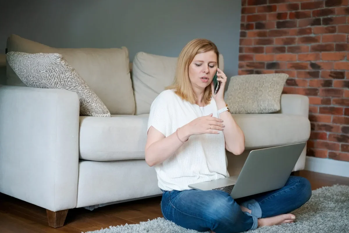 žena s notebookem na klíně telefonuje