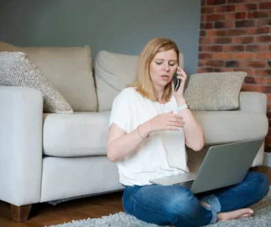 žena s notebookem na klíně telefonuje